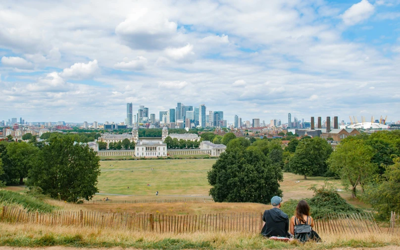 a couple sits on the edge of a hill looking at the city