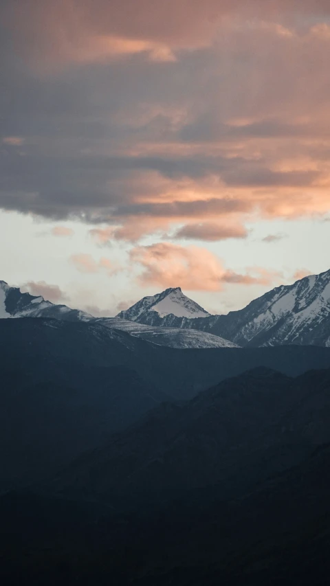 snow covered mountains under a cloudy sky at dusk