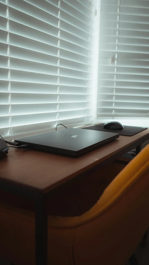 a small laptop is on a desk in front of window blinds