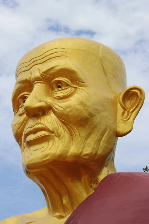 a large golden head statue in the middle of a park