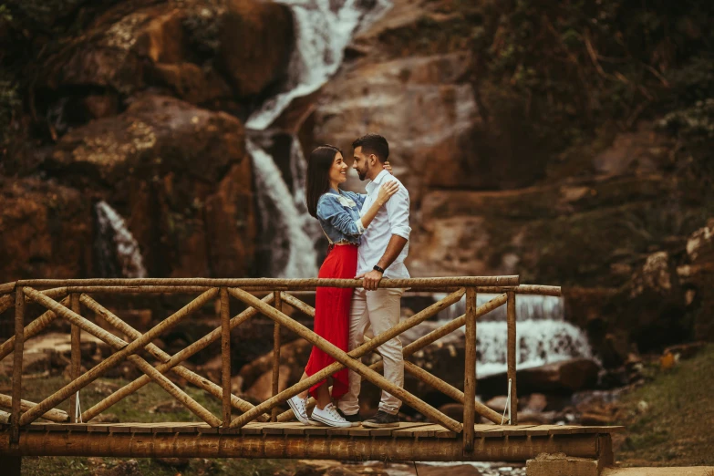 a man and a woman emcing as they stand on a bridge that spans a waterfall