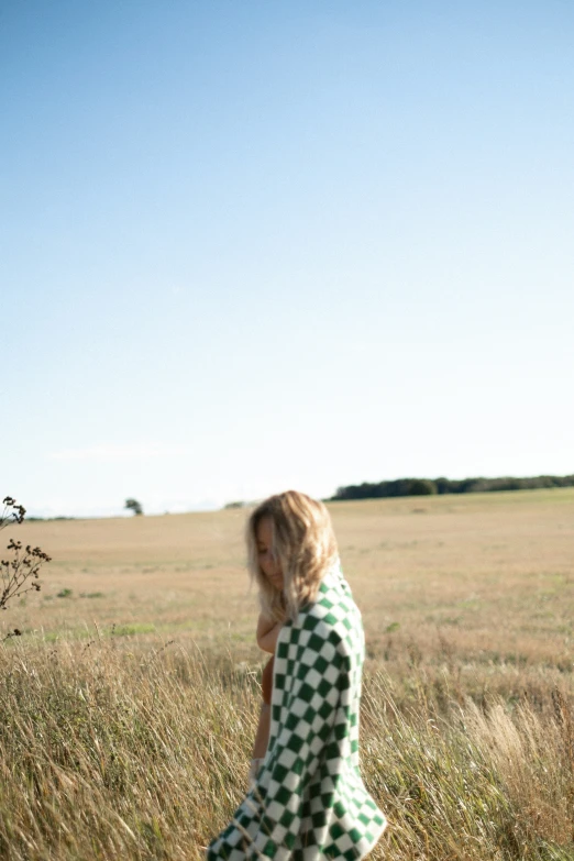 a girl in green and white dress walking through grass