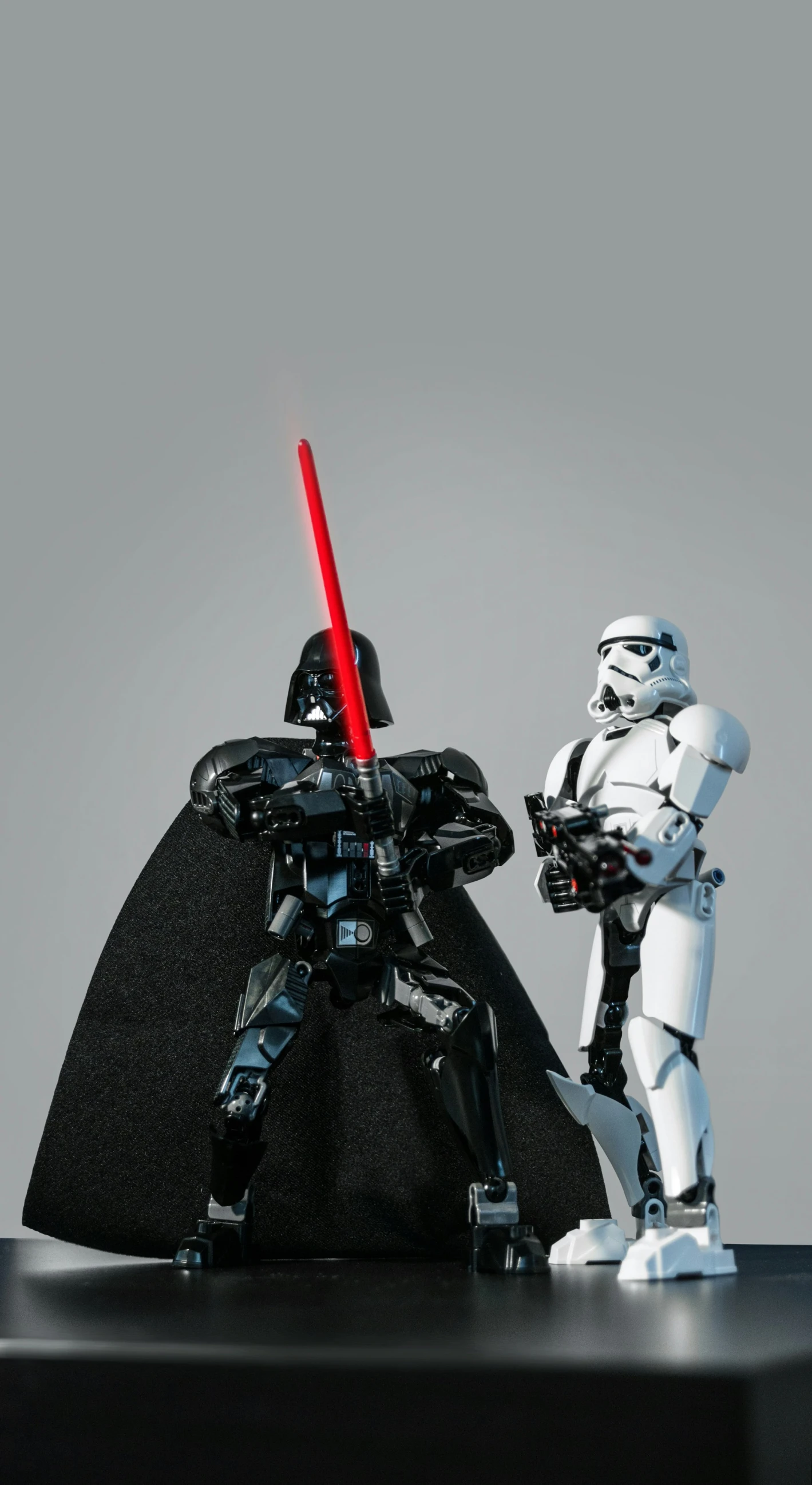 a robot next to a sit - down stormtrooper in front of a black rock