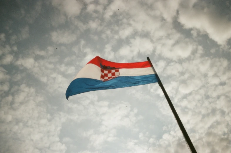 a red and blue flag on a pole with clouds in the background