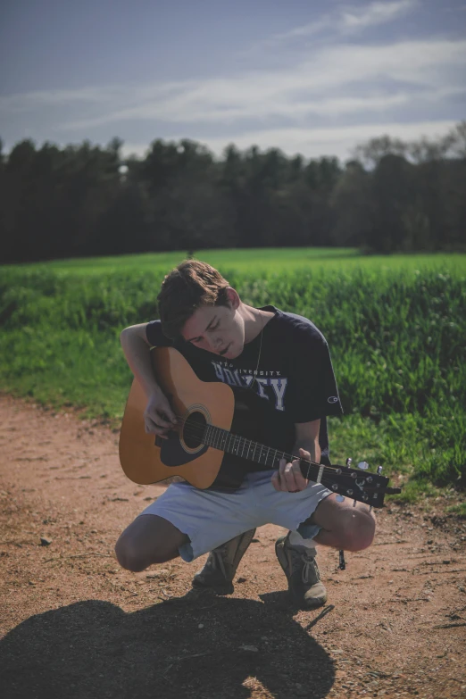 a person kneeling down with a guitar on a dirt road