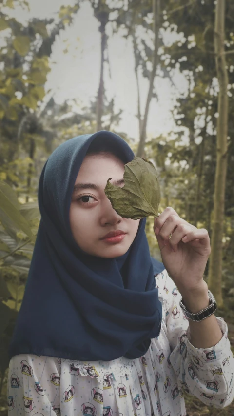 a young lady wearing a headscarf holding up a leaf