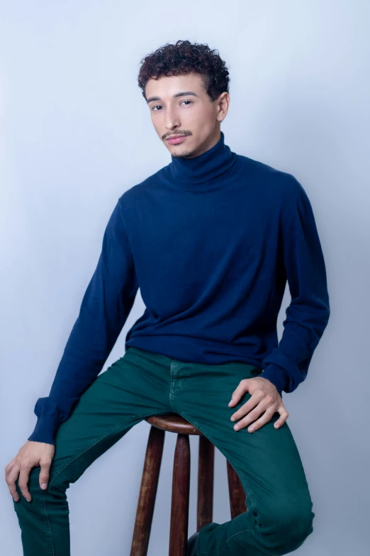 a man in a turtle neck sitting on a stool