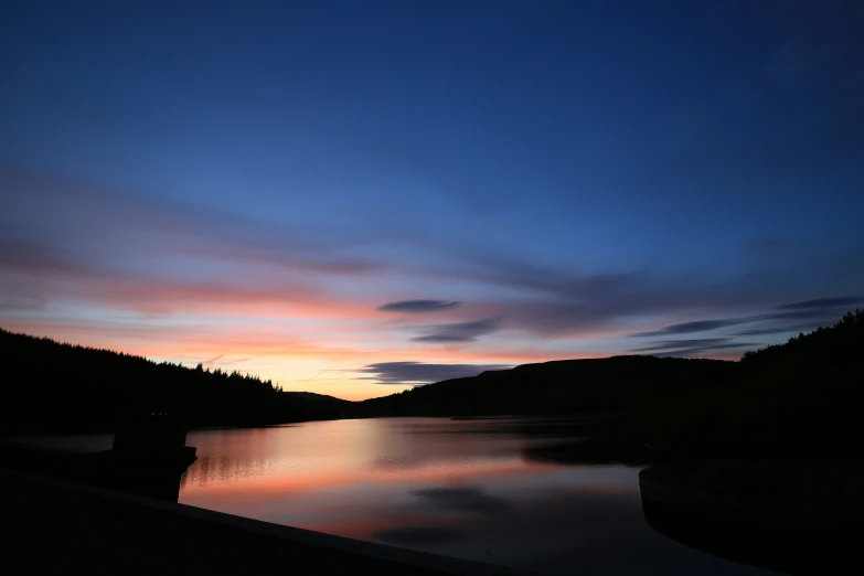 a dark sky and the sun is setting over water