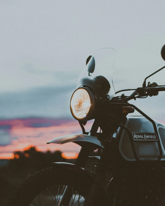 a motorcycle parked in a field with the sunset behind it