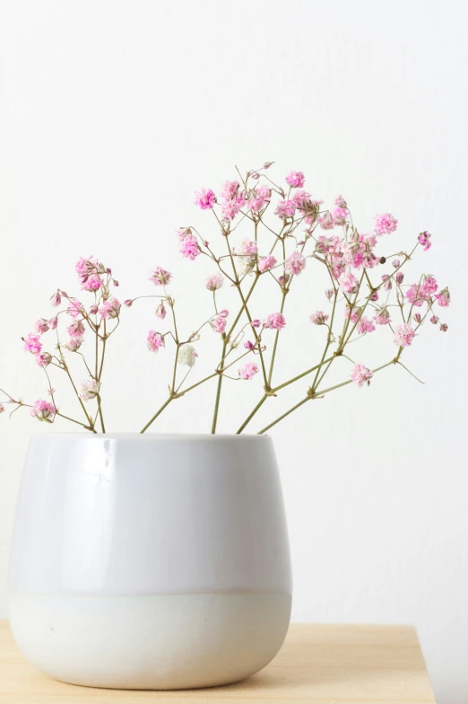 pink flowers in a white vase sitting on a wooden table