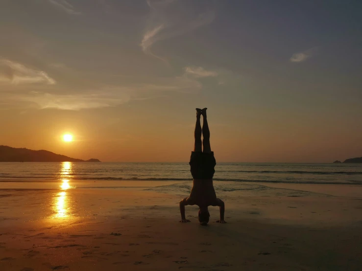 a person stands in the sand doing a handstand