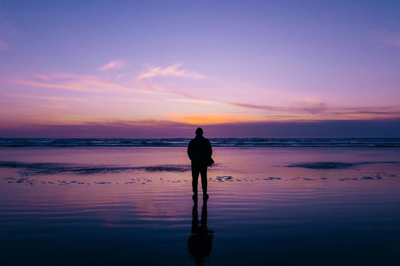 man standing on beach at sunset with reflection in water