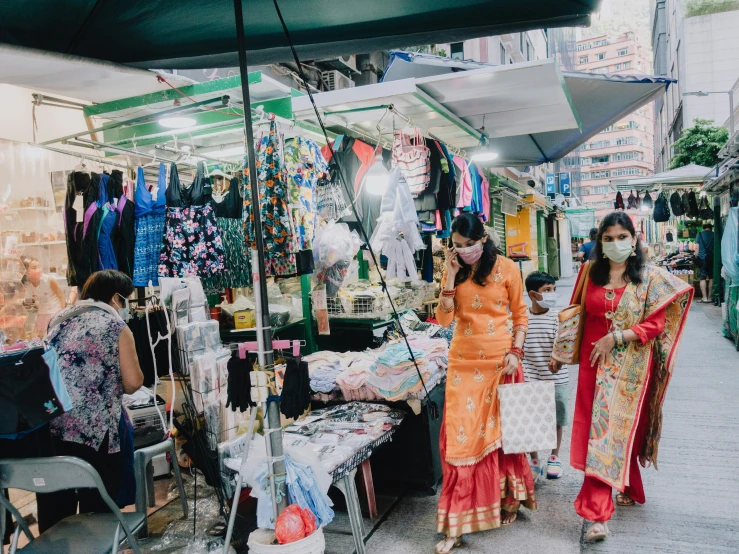 two women are walking by a small booth selling clothing