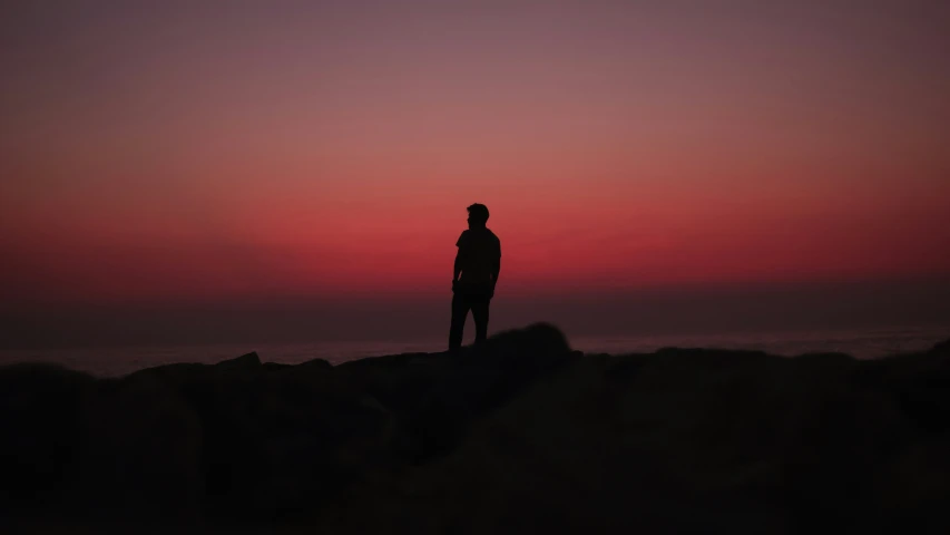 silhouette of man standing on rocky area near ocean