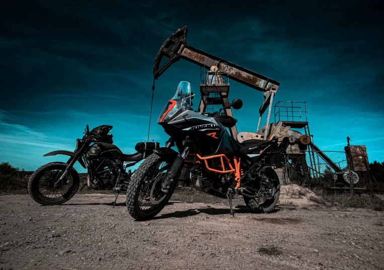 two motorcycles sit parked in front of an old oil pump