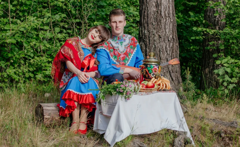 a man and woman in costume sitting at a table in the woods