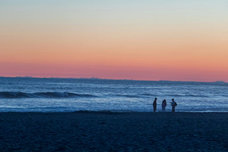 three people stand on the beach while sun sets