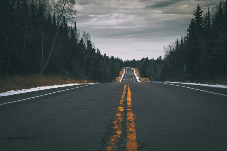 an empty highway in the woods with a cloudy sky