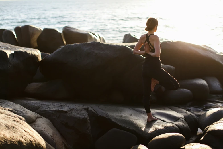 woman doing yoga next to rocks on a beach