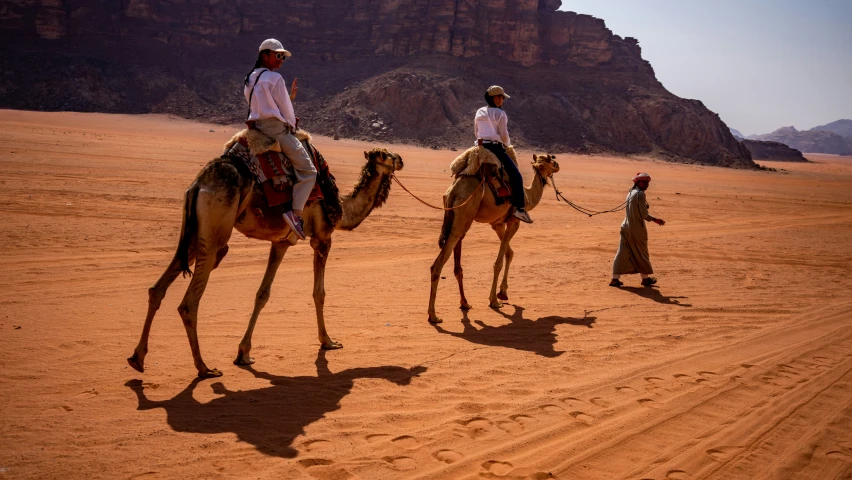 two men riding camels across a sandy desert plain