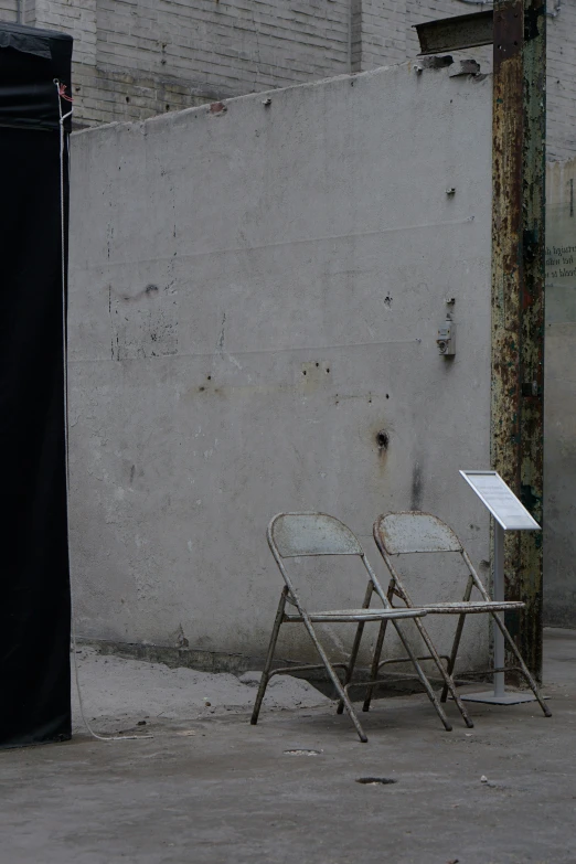 two folding chairs are on the street by a wall