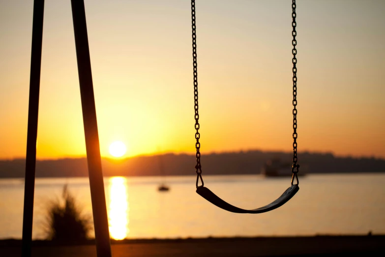 an empty swing at sunset or sunrise over a body of water