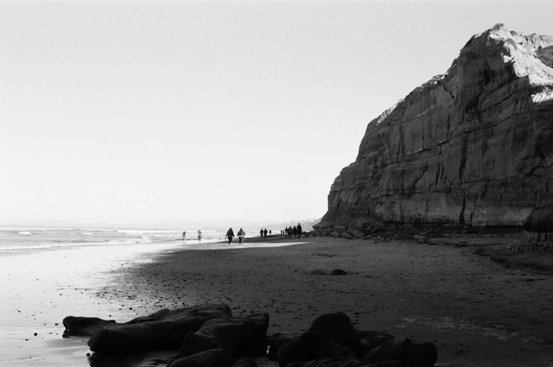 a black and white po shows people walking on the beach in front of a mountain