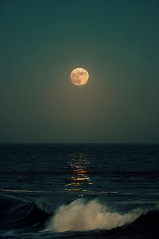 the full moon shining over the ocean water