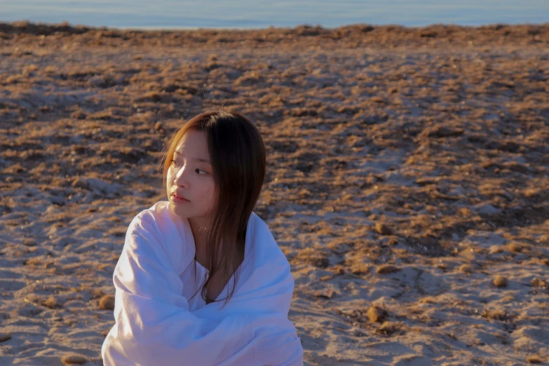 a beautiful woman wrapped up and sitting on top of a sandy beach