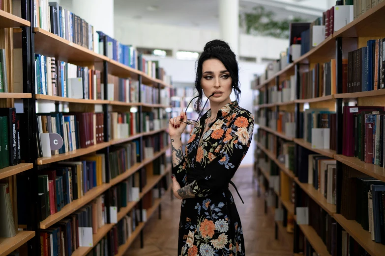 a beautiful young woman standing in front of a book shelf holding an object