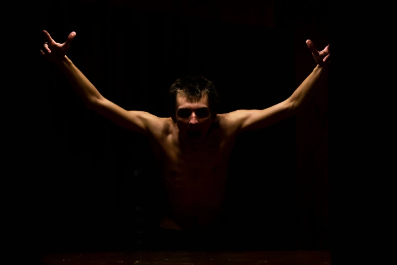 a man is shirtless in the dark, with one arm outstretched out