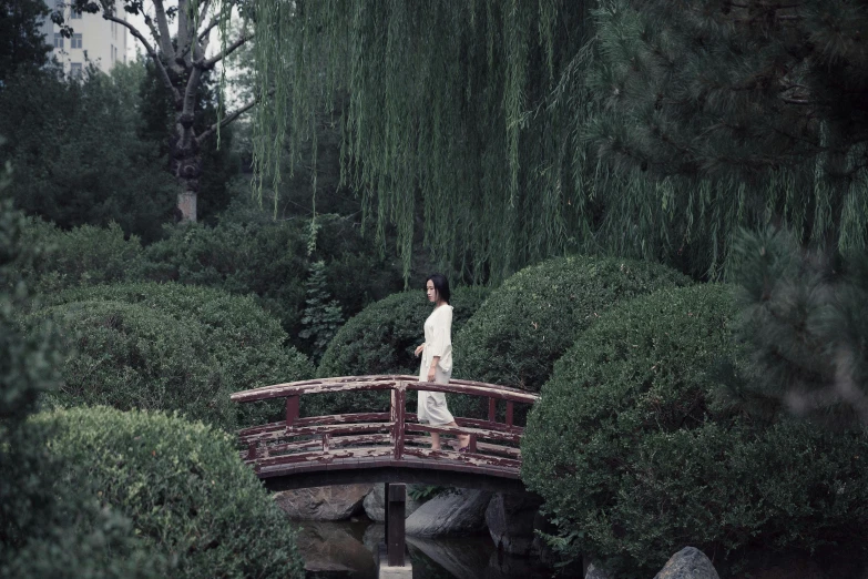 an asian woman stands on a red bridge near water