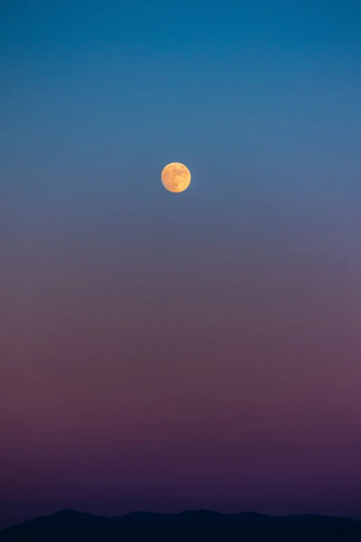 a full moon in the sky with hills below