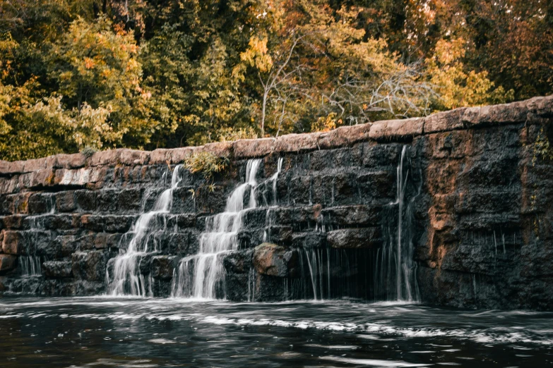 there is a small waterfall running over a stone wall