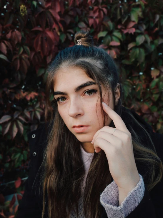 a girl in a jacket is posing with her finger on her head