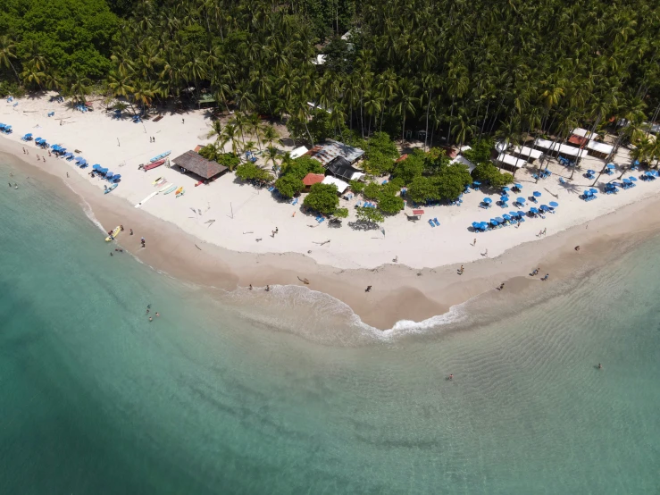 an aerial view of a beach with blue umbrellas on the shore and several small boats parked out on the sand