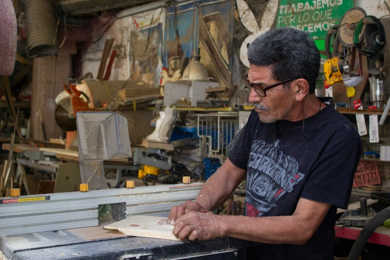 a man with glasses and black shirt working on a piece of wood