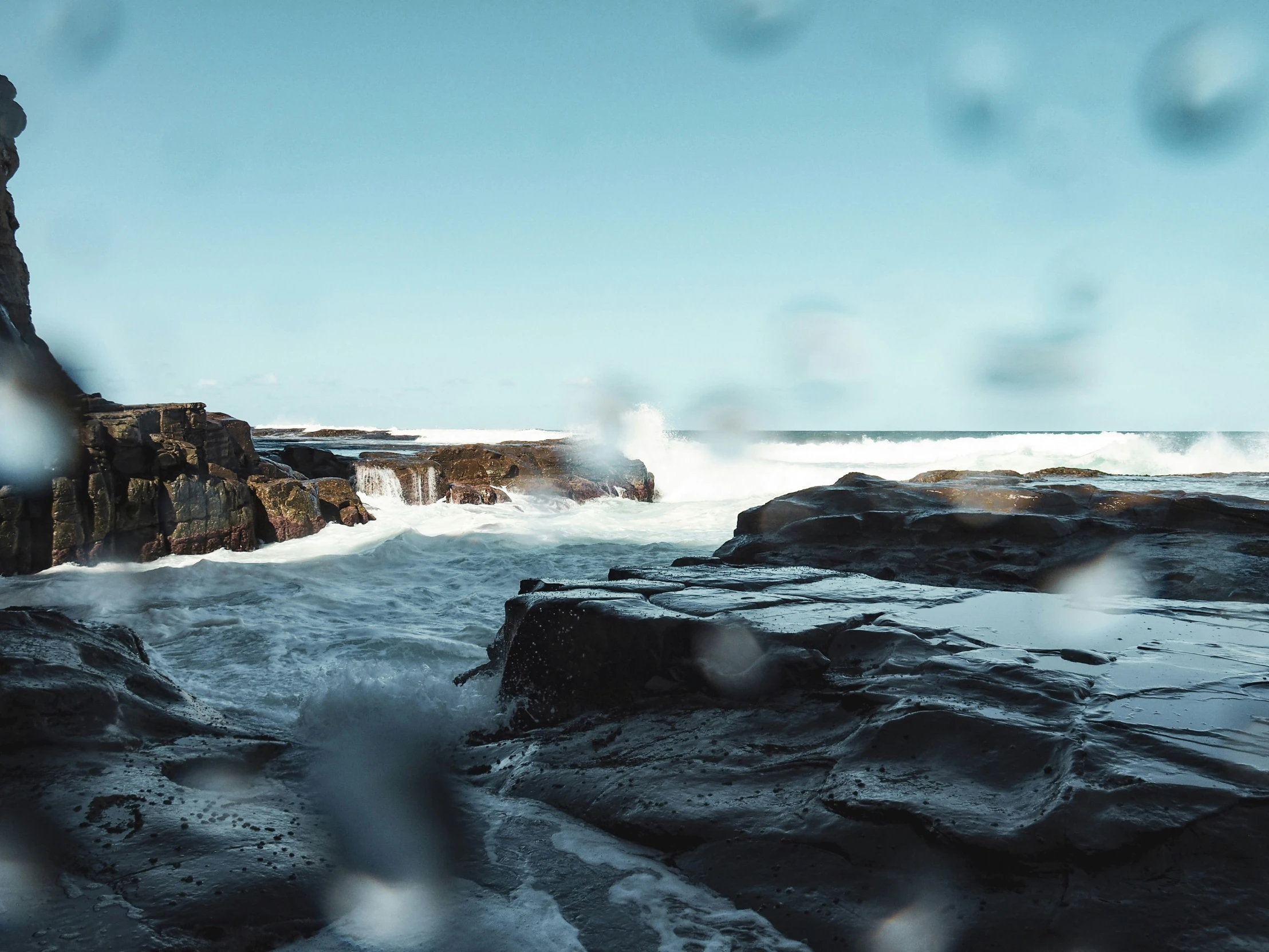 the view out through water drops onto rocks near the ocean