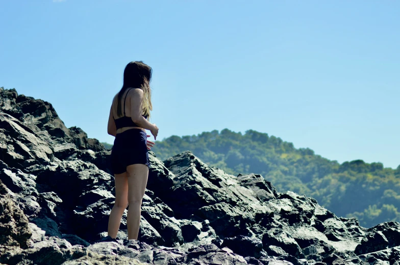 a woman in short shorts standing on top of a rocky hillside