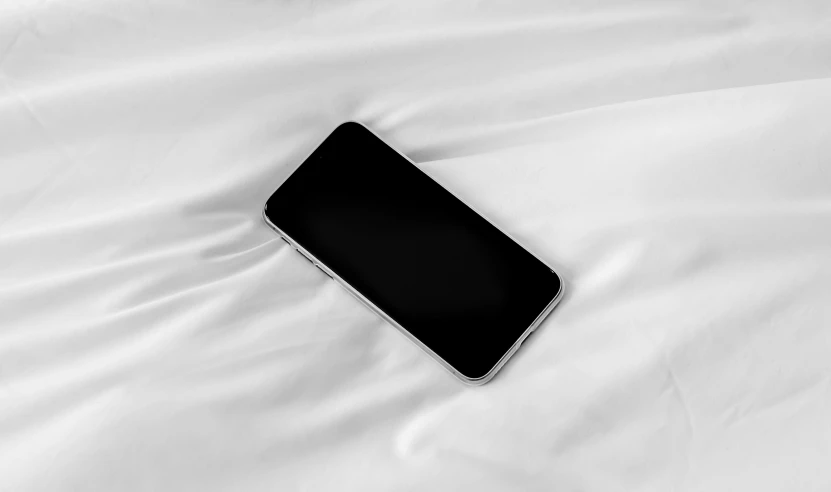 a black cellphone lying on a white bed sheet