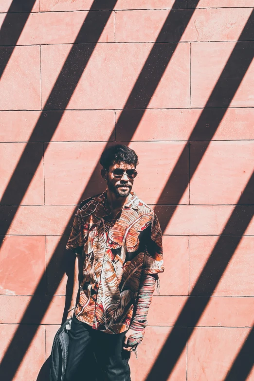 a man standing in front of a pink wall holding a purse