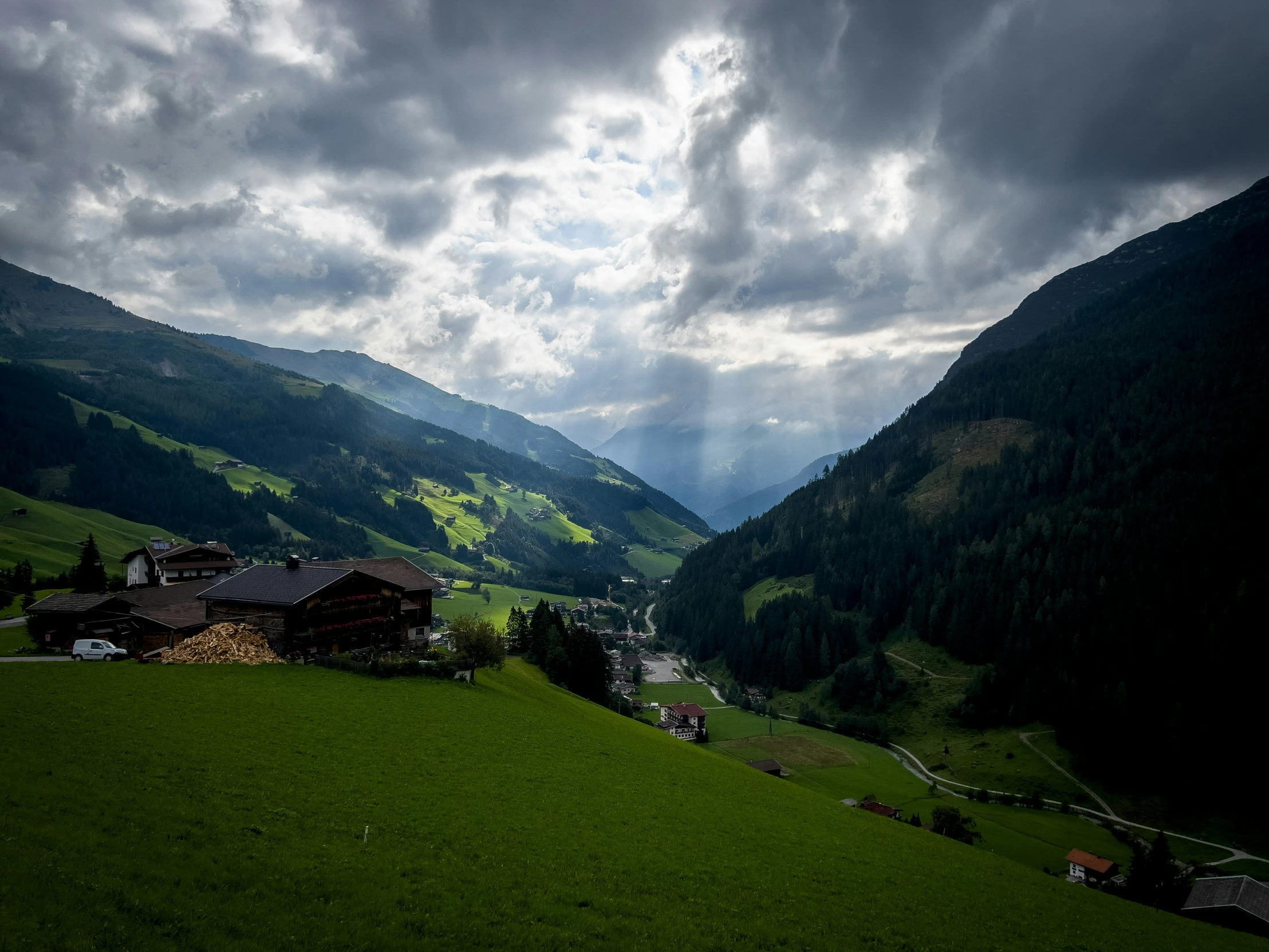 a green hillside with a house in it and trees under a cloudy sky