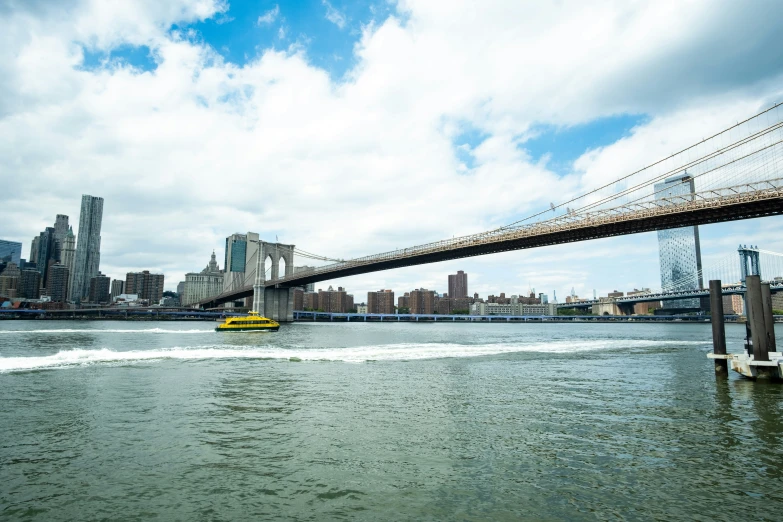 the yellow boat is going under the suspension bridge