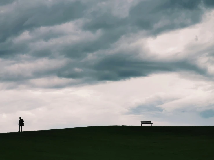 a lone person stands on the top of a hill with a sky filled with storm clouds