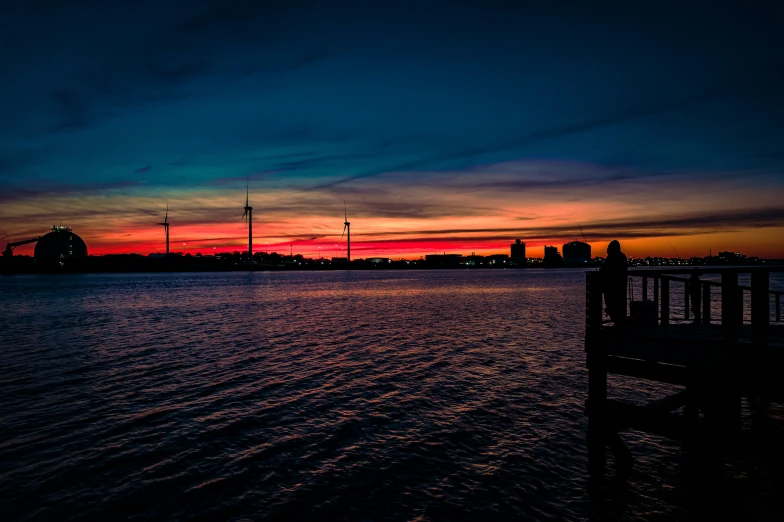 a red sunset reflects on the water next to a pier