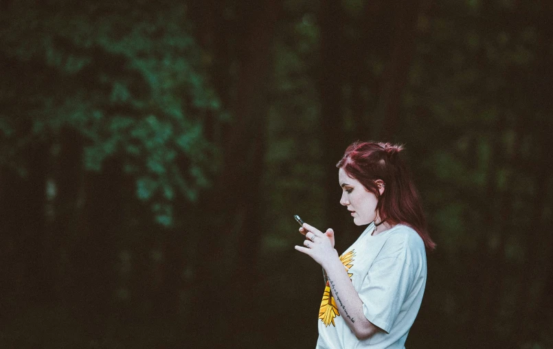 a woman standing on the side of a forest holding a cell phone