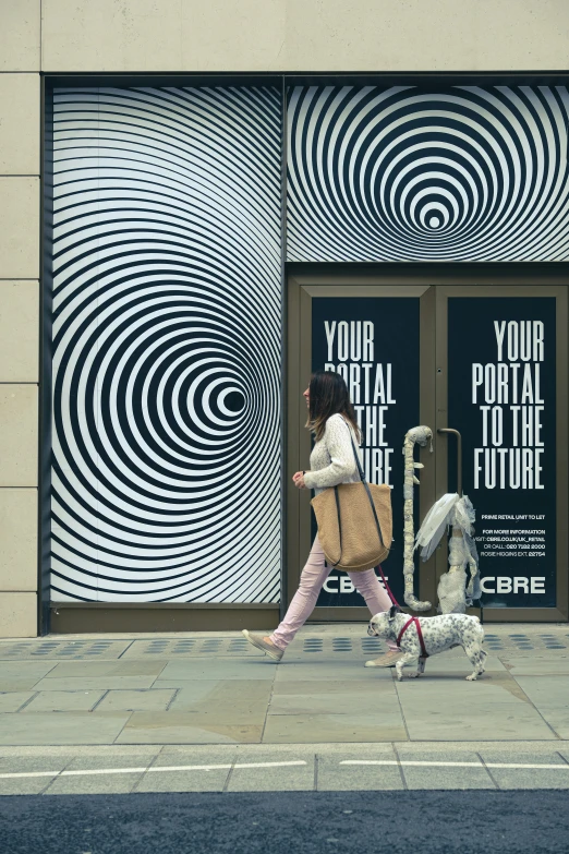 a woman walking a poodle down a sidewalk past a store front