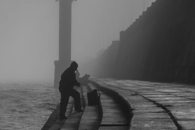 black and white image of man standing at edge of ocean in fog