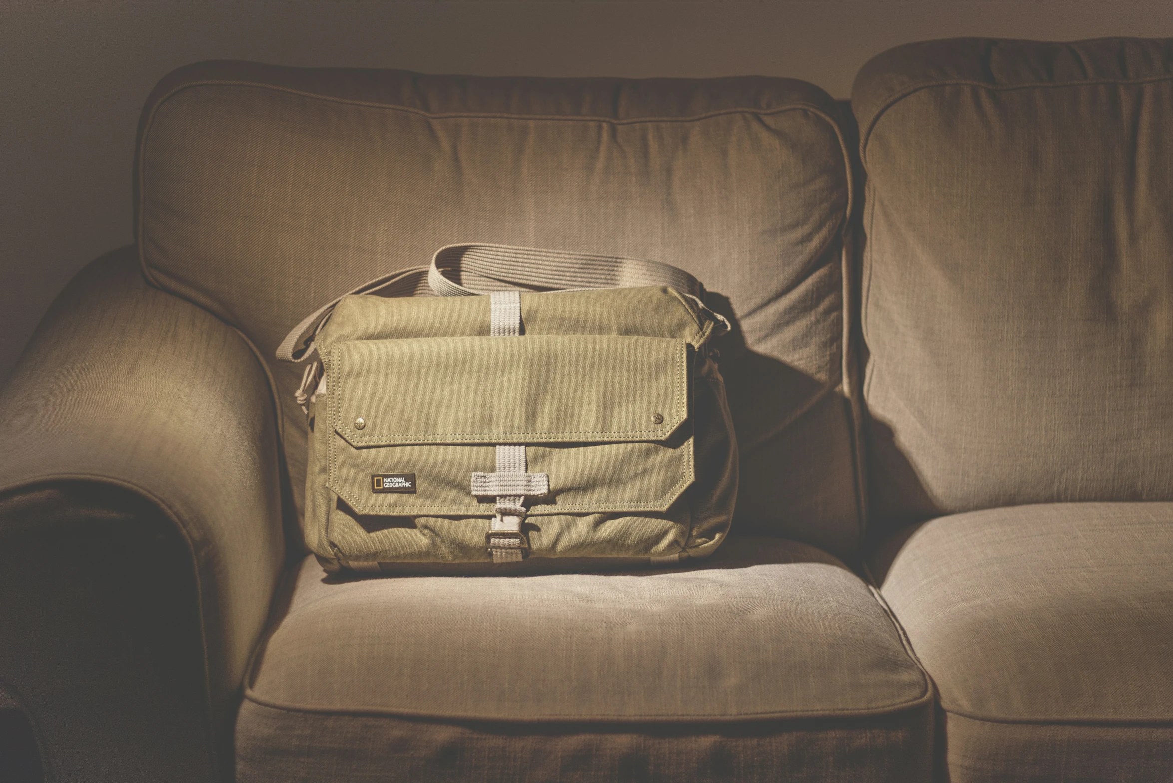 a tan backpack sitting on a couch in front of a gray wall