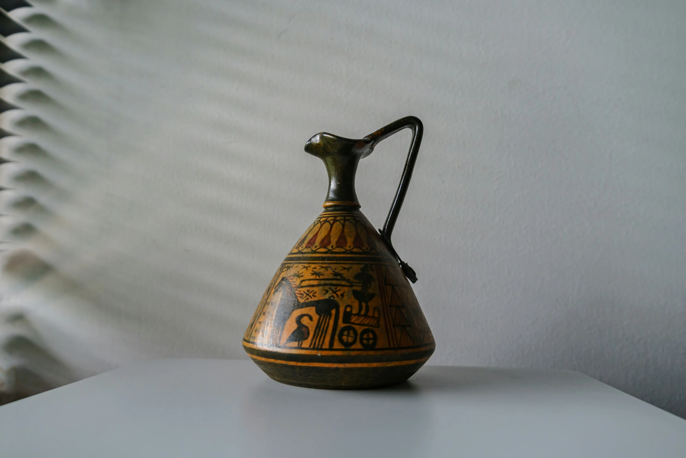 an empty vase with writing on it sitting next to blinds